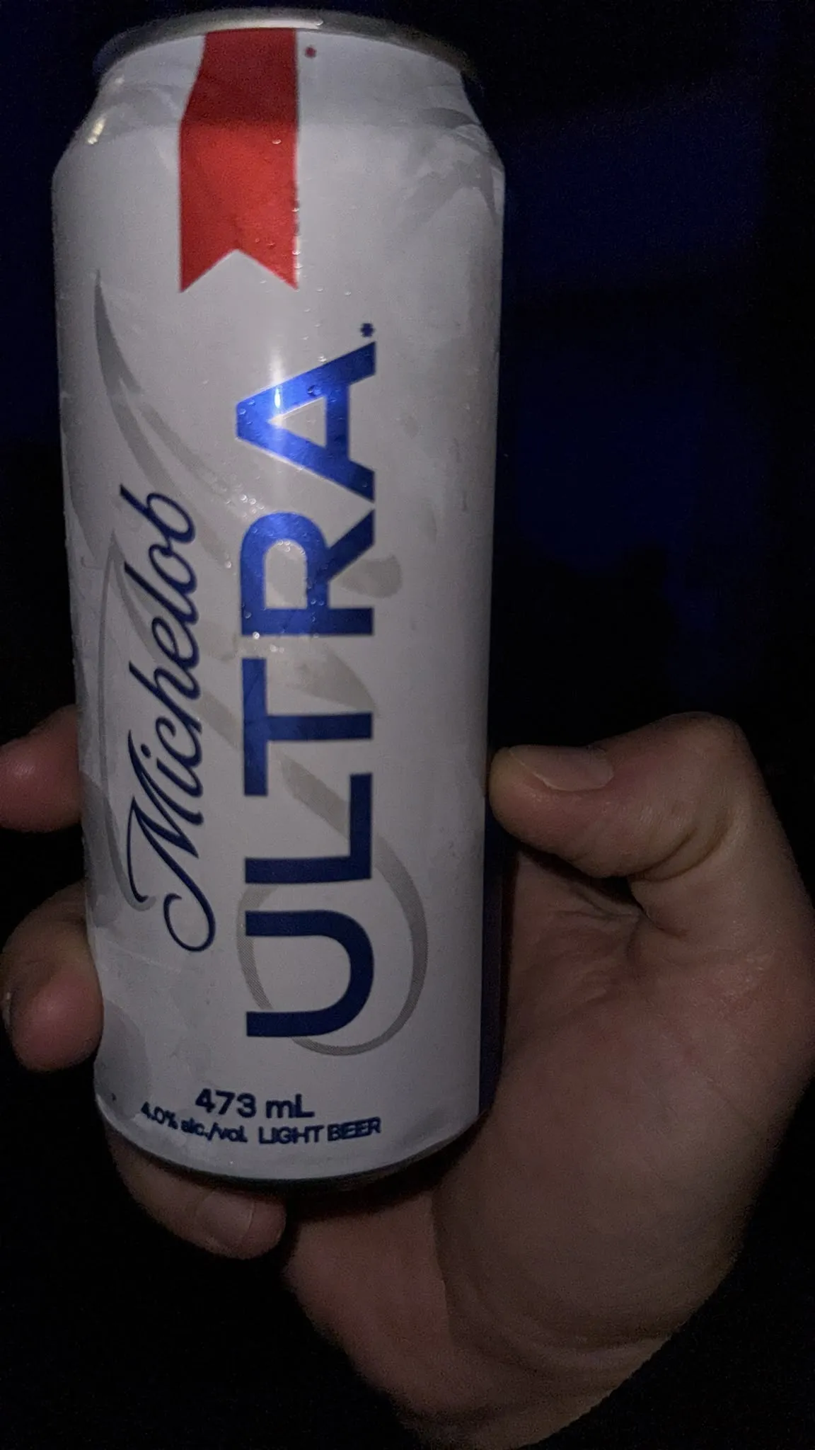 A frosty Michelob Ultra tallboy held up close against a dark night background.